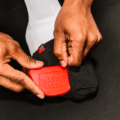 Close-up of hands inserting a red Crease Beast shoe crease protector into a black shoe.